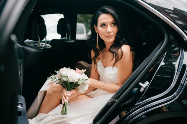 A bride in white dress sitting in black limousine